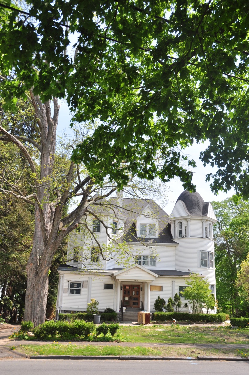 White New England Victorian framed by a mature shade tree
